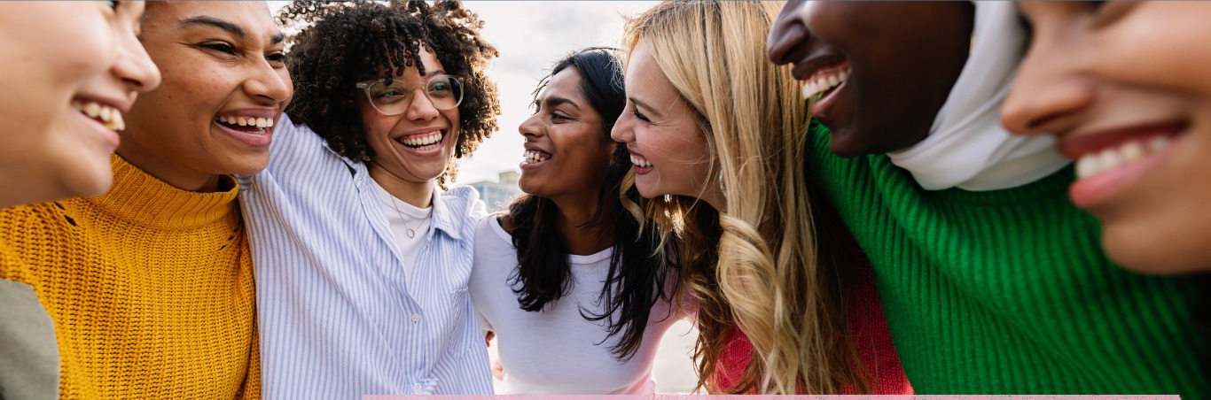 A close circle of women laughing together outdoors, arms around each other